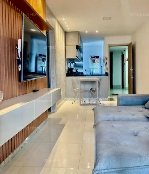 Sala com sofá azul, painel de TV ripado e cozinha americana ao fundo