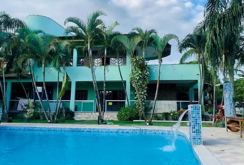 Casa de dois pavimentos com piscina e cascata, cercada de palmeiras